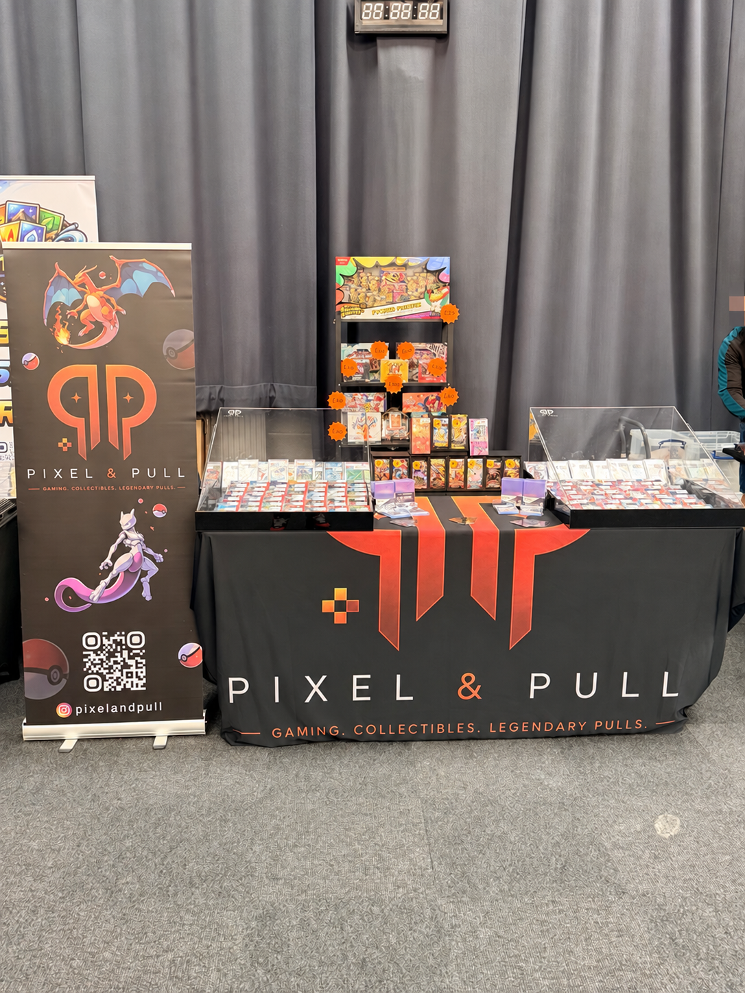 Pixel & Pull orange and black card show stand; visible face pixelated for privacy